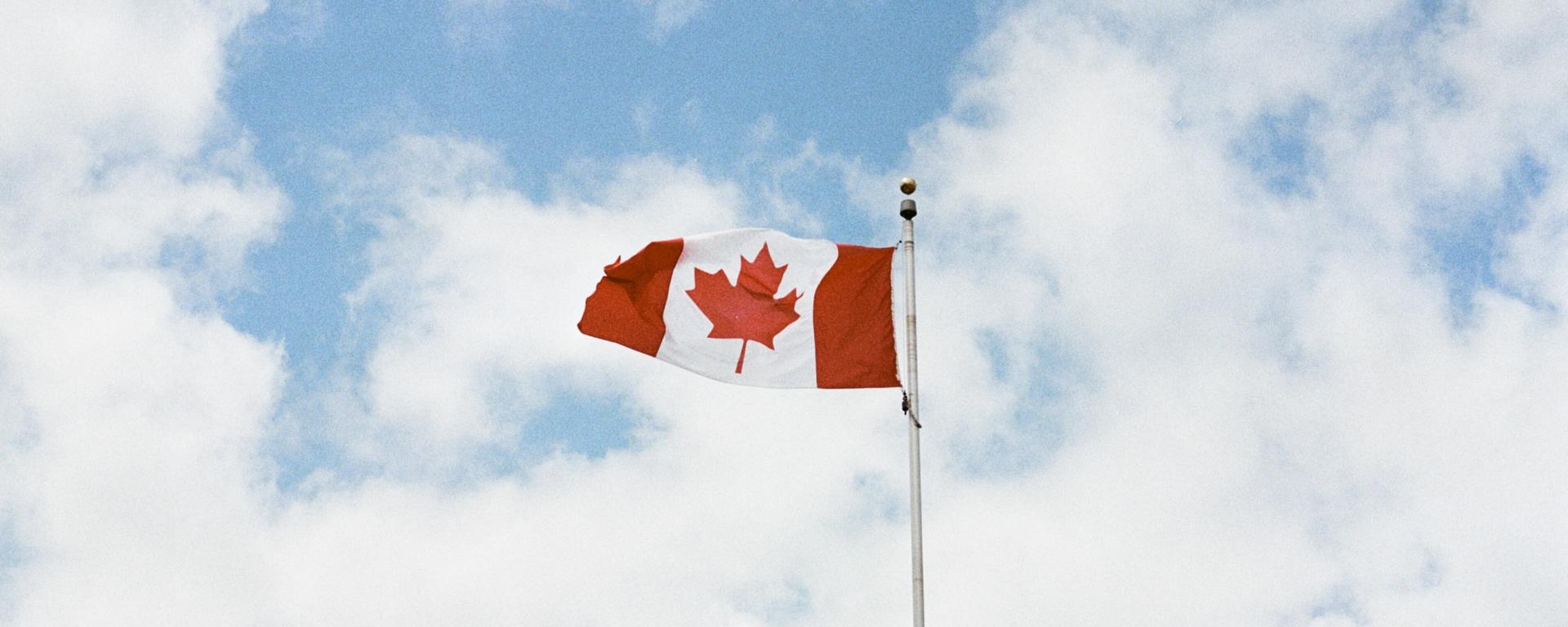 A Canadian flag flies proudly against a partly-cloudy sky