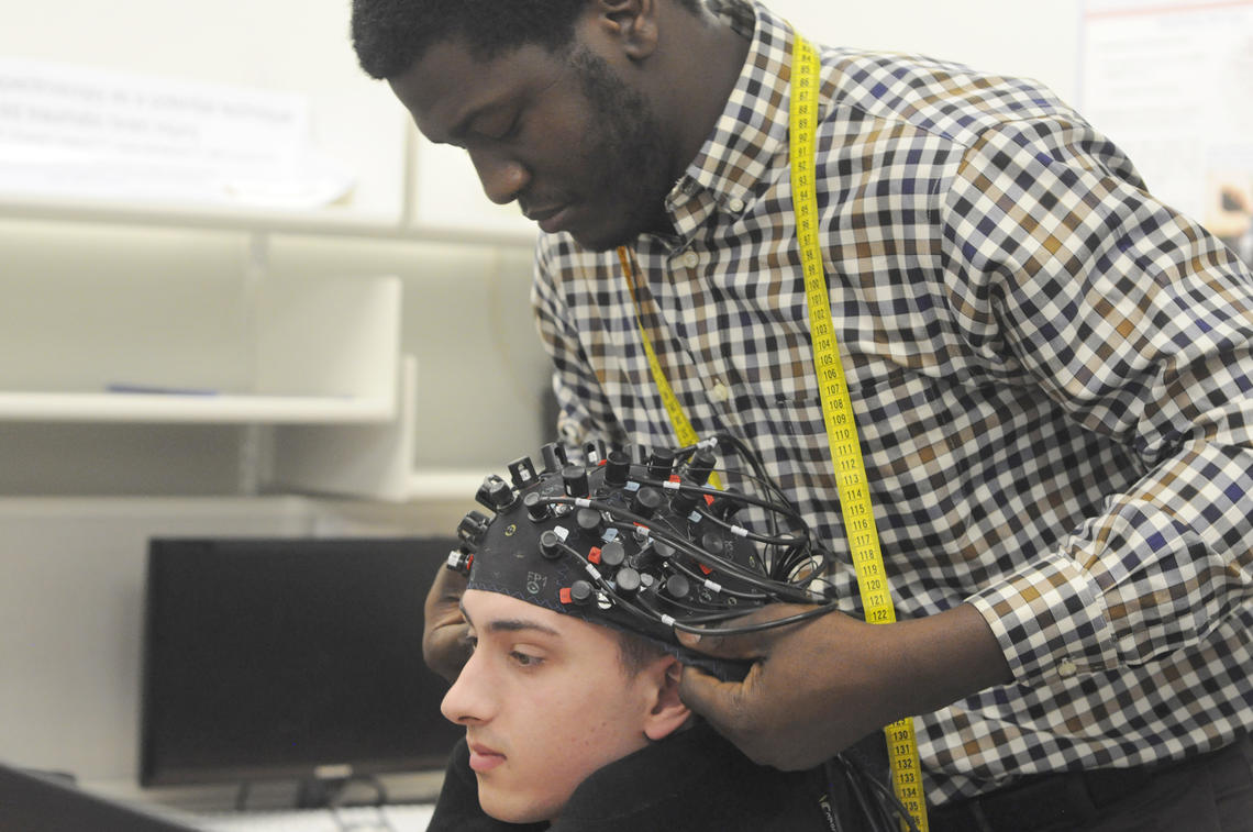 Ibukunoluwa Oni places the brain imaging cap, which contains LED lights that illuminate the skull and allow researchers to monitor and measure brain activity.
