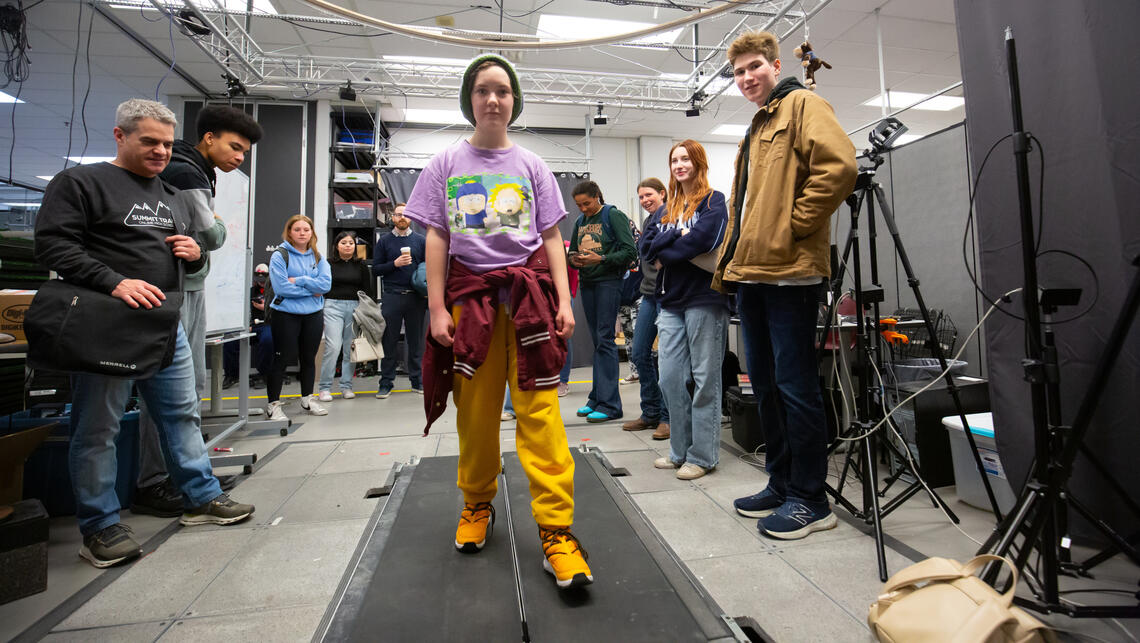 A young girl walks on a treadmill while others watch