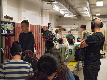 People gathered in a locker room with a film crew