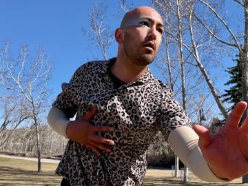 A dancer wearing a leopard print shirt gestures in a field