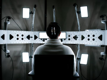 Back of human figure facing a series of monitors and other technology