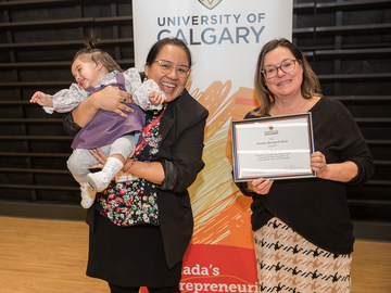 Ana holds her daughter and is presented with a certificate by Katrina Milaney
