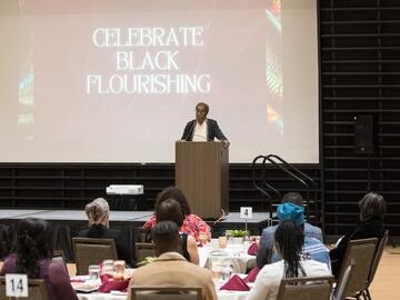 : Dr. Smith presents during ceremony in front of screen that reads, ‘Celebrate Black Flourishing’