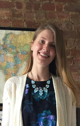 Alumna Alexandra Kennedy smiles in front of a brick wall with a map poster on it