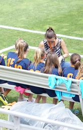 Coach talks to sports team on sidelines of field