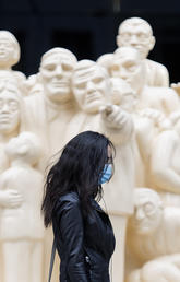 A woman wears a face mask as she walks by the sculpture ‘The Illuminated Crowd’ on a street in Montréal. 