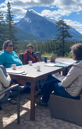 People sit around a table outside with a mountain in the background 