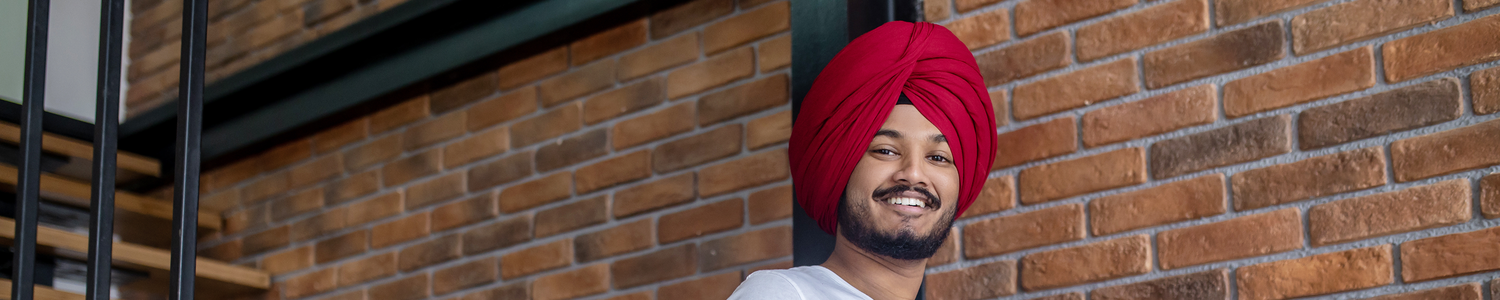 Stock image of a smiling young man in a turban walking down stairs with his laptop