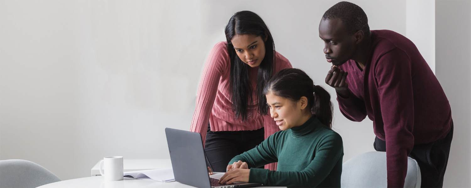 Three students look at a laptop together. Stock photo.