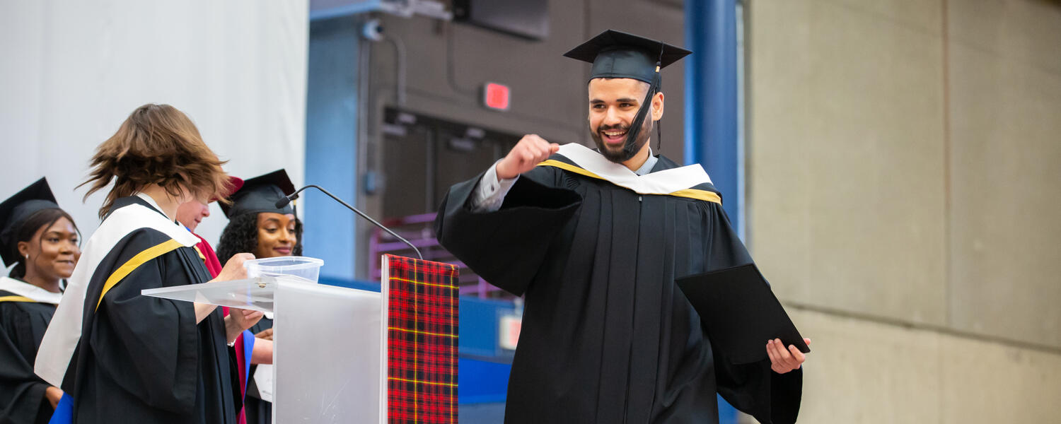 A student fist bumps the air in celebration as he crosses the stage at convocation.