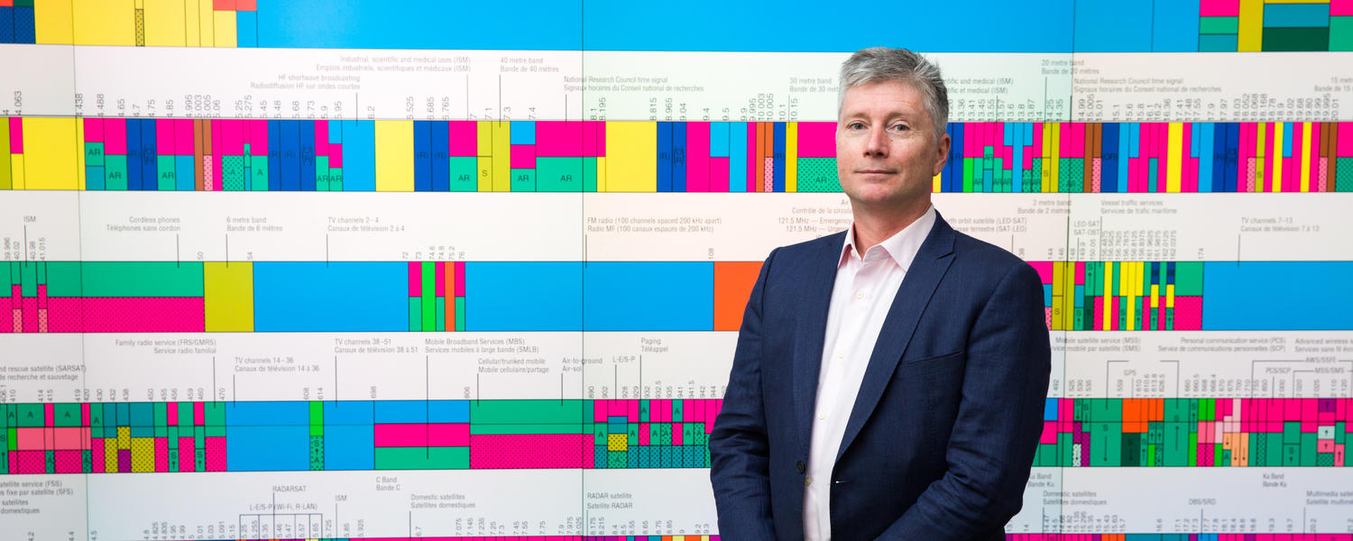Communication, Media and Film Researcher Gregory Taylor stands in front of a wireless spectrum graph