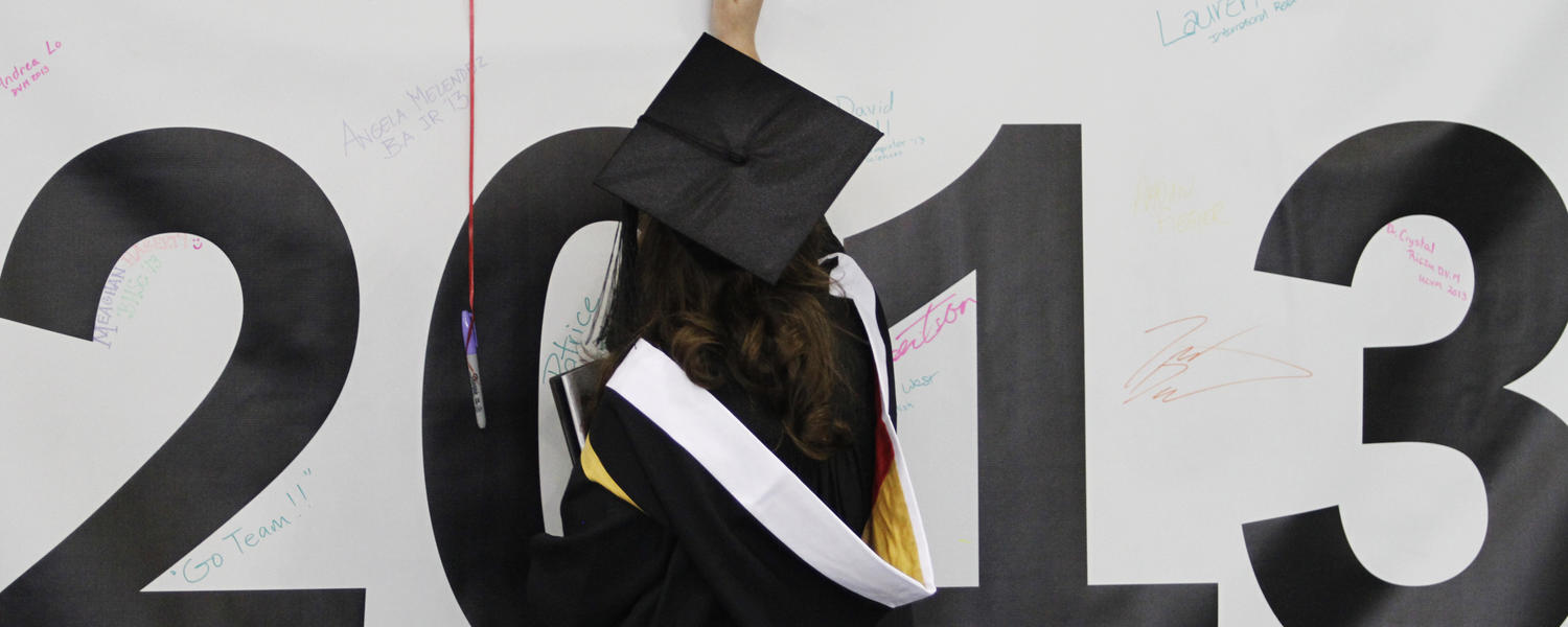 A graduate signs a large banner with "2013" in large black letters