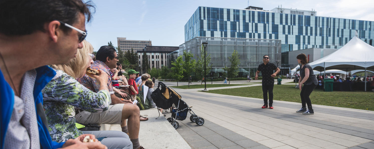 Alumni and families enjoy a sunny day while they watch an outdoor presentation at Alumni Weekend