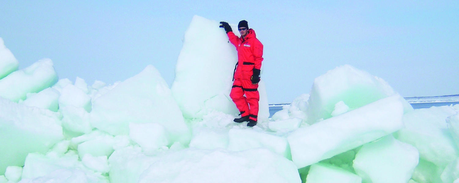 Geography researcher Brent Else stands on top of iceberg rubble. He is wearing a full snowsuit, gloves and toque.