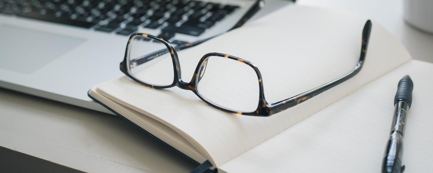 Desk with a notebook, glasses and a computer on it