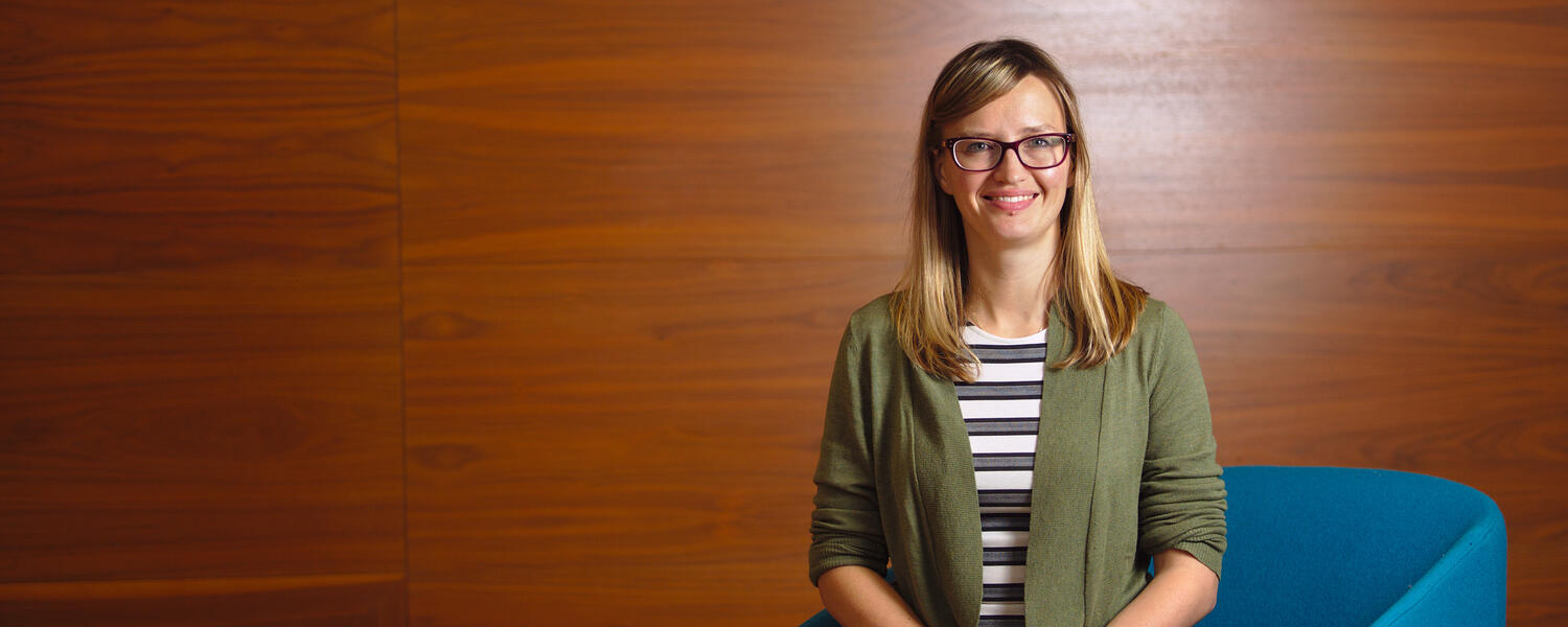 Dr Amanda Melin sitting on a blue chair with a wooden background