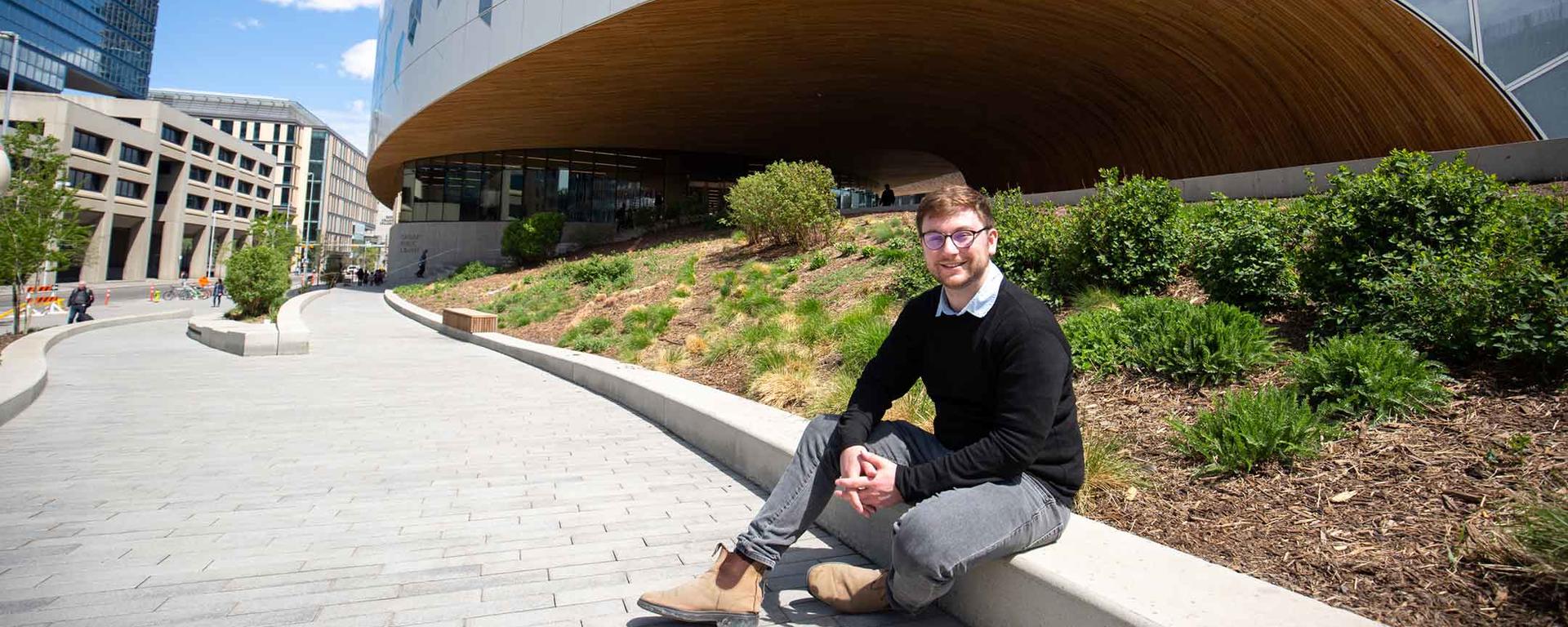 Russell Copley, MSc Geography, sits in front of Calgary's main library branch