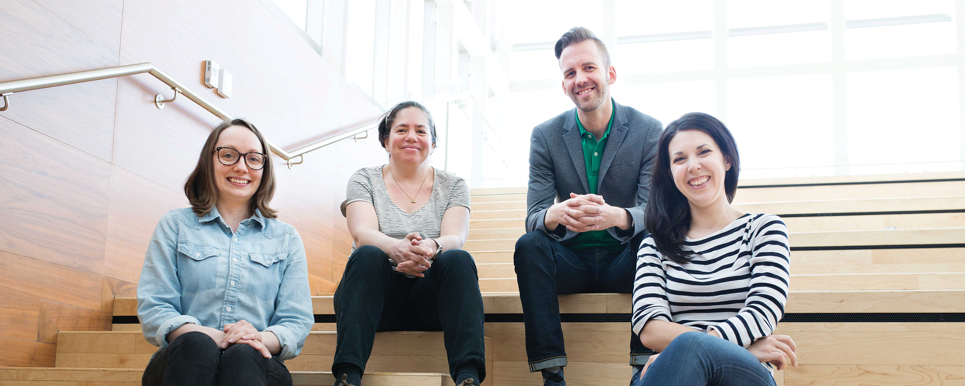 Four people sit on a bleacher style stairs. They're all smiling and relaxed.