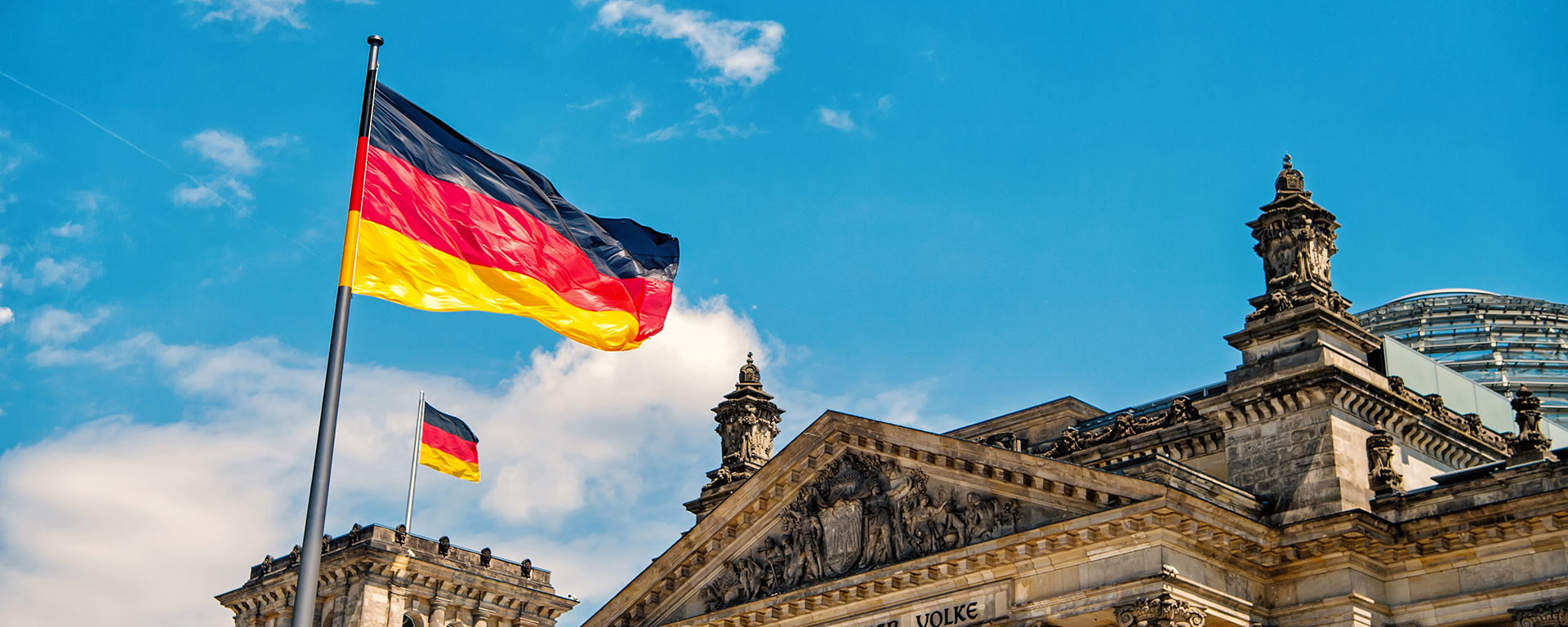 German flags waving in the wind at famous Reichstag building, seat of the German Parliament Deutscher Bundestag , on a sunny day with blue sky and clouds, central Berlin Mitte district, Germany