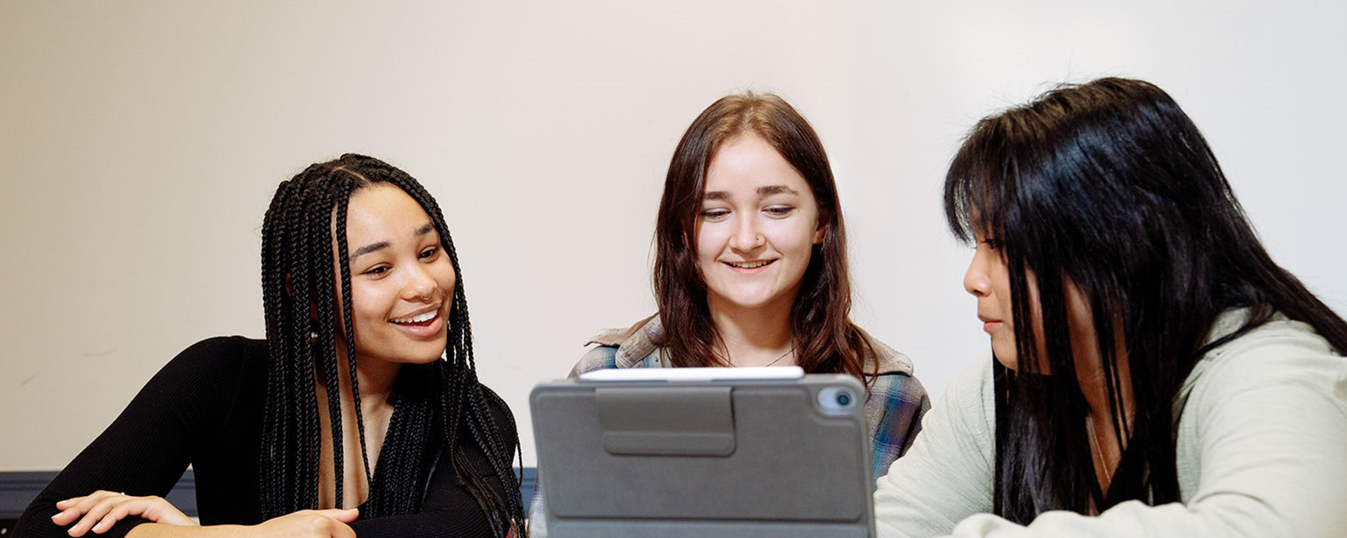 Three female English undergraduate students from different ethnic backgrounds look at a laptop together in a classroom.