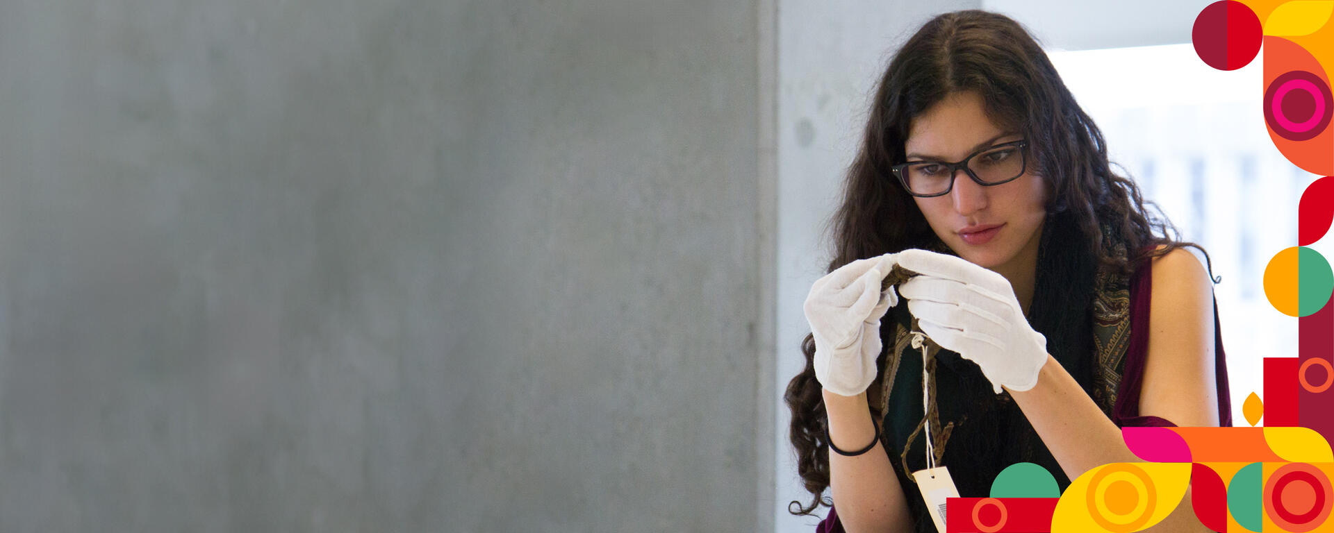 A student wearing protective gloves examines an artifact.