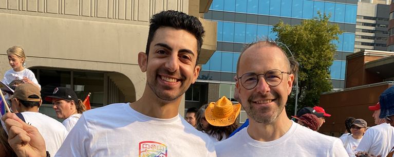 Two faculty members at the Pride Parade. They're wearing UCalgary Pride shirts.
