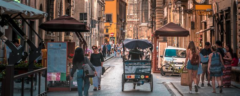 A narrow street in Florence, with a few tourists and cars on the road