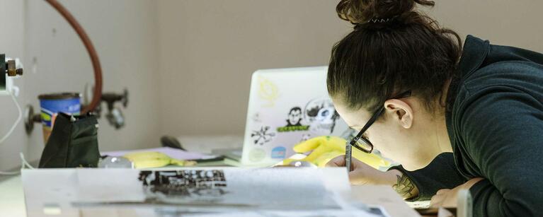 An art student bends over their work at a drafting table