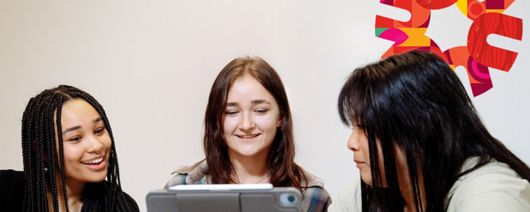 Three students of diverse ethnic backgrounds collaborate together in a classroom. They are looking at a tablet together. The UCalgary Arts spark appears in the background.