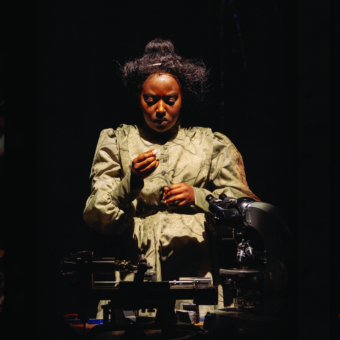 An actor peforms on stage. She is brightly lit and the area around her is dark.