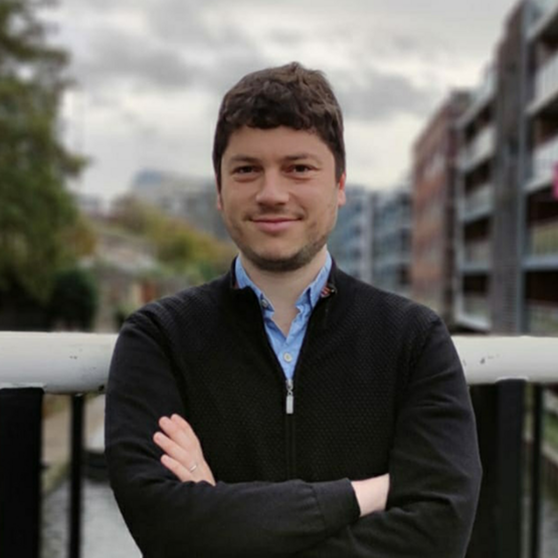 Dr. Noam Titelman, a white man, stands outside in an urban area. His arms are crossed and he is smiling.