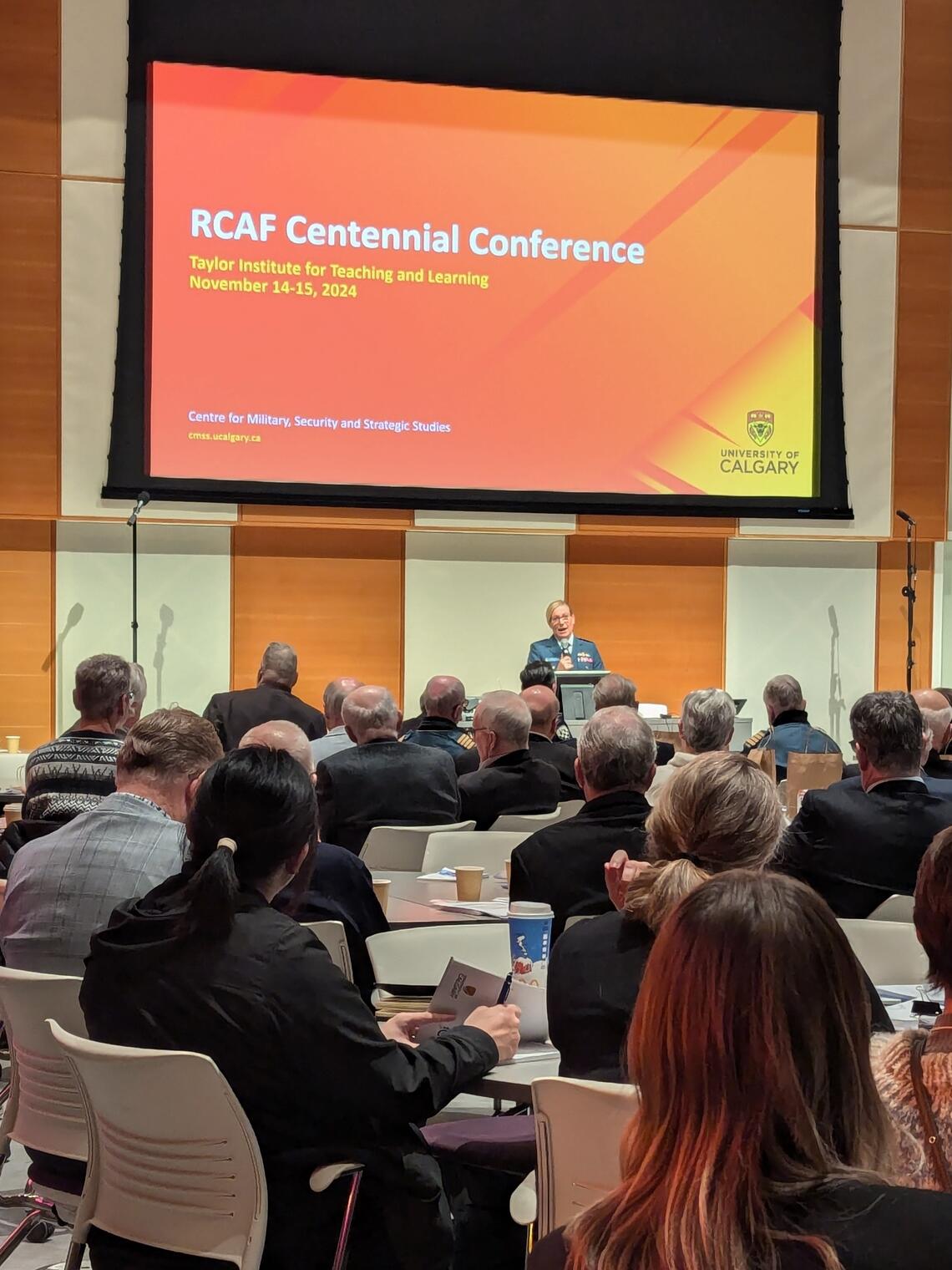 crowd seated at round tables looking at screen reading "RCAF Centennial Conference"