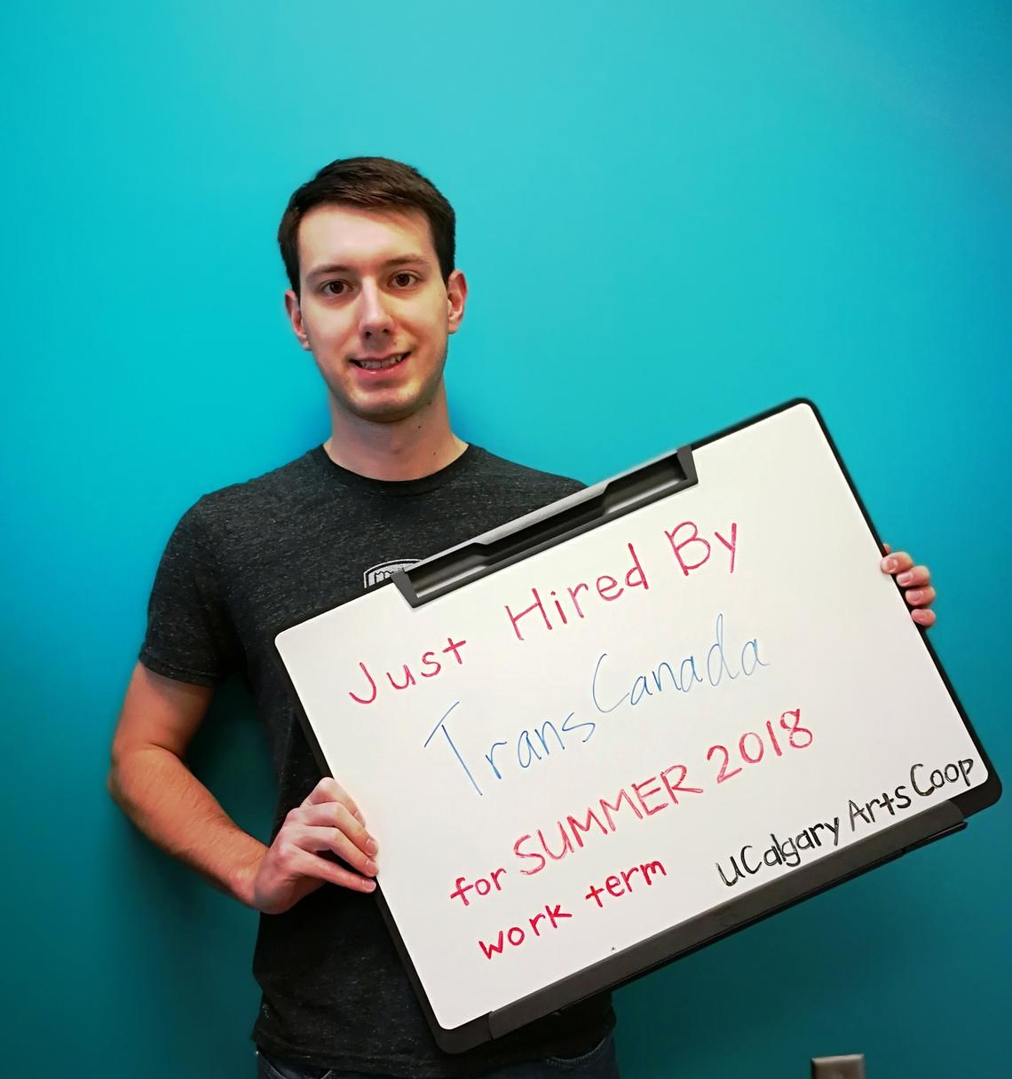A student holds a signboard that reads "Just hired by TransCanada for SUmmer 2018 work term"