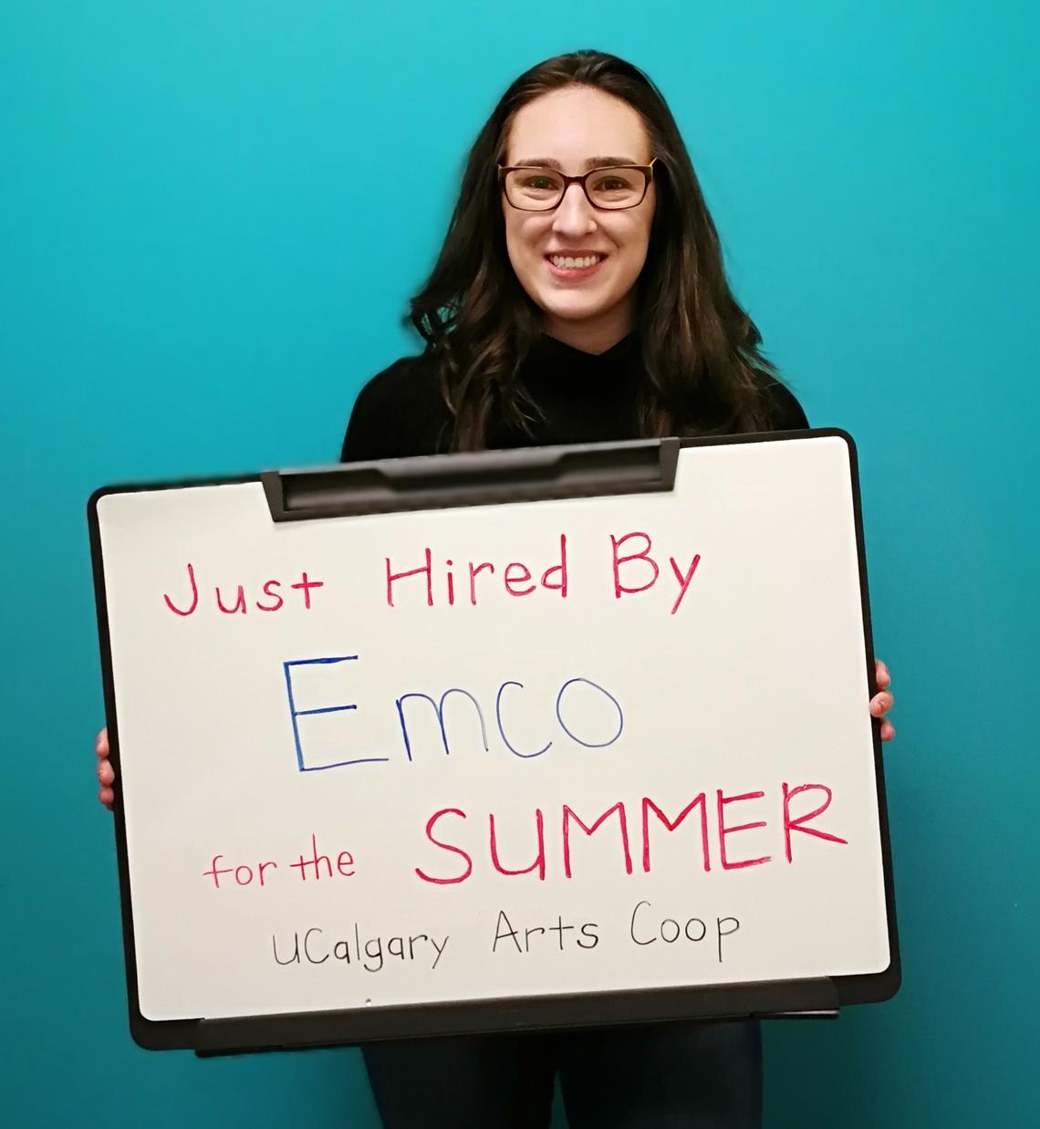 A student holds a signboard that reads "Just hired by Emco for the Summer"