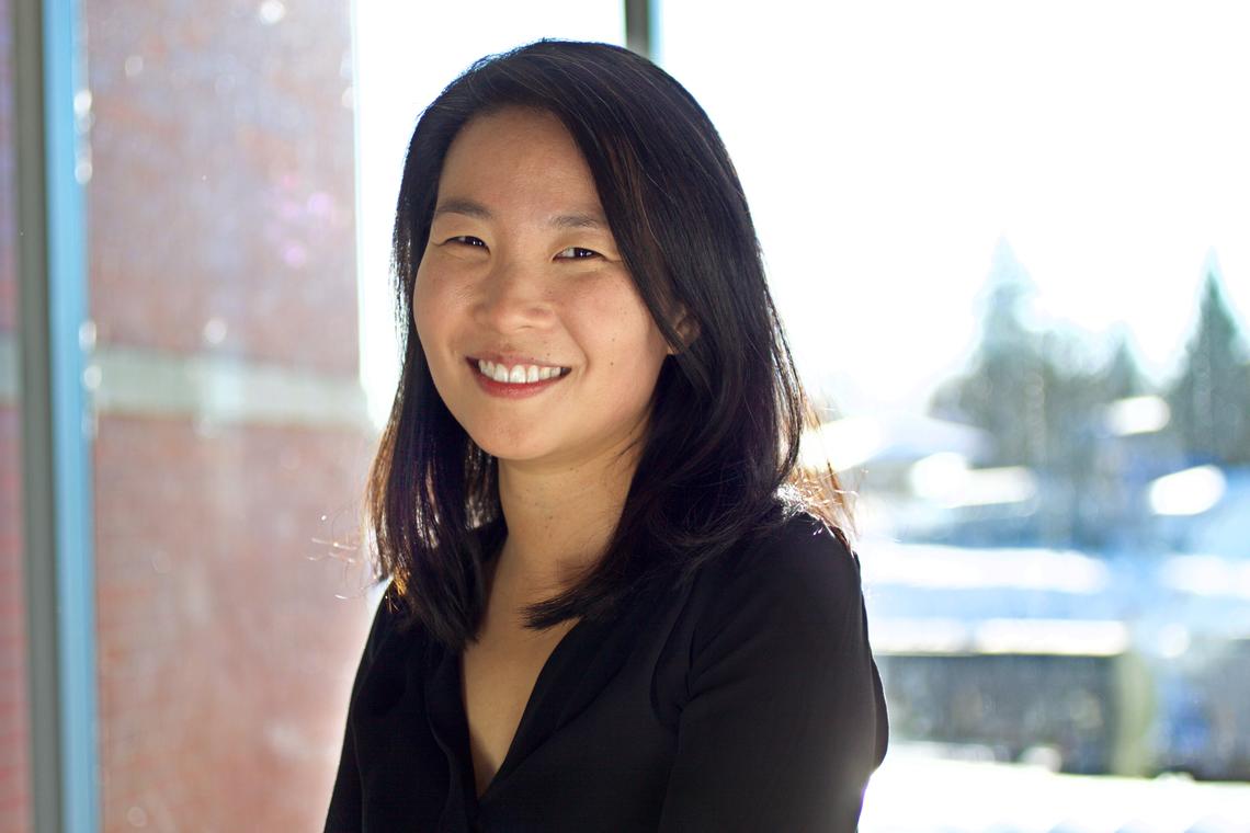 2021-22 Canadian Writer-in-Residence Teresa Wong Teresa Wong stands in front of a sun-filled window. She smiles at the camera and wears a black v-neck shirt with long sleeves and her hair loose.