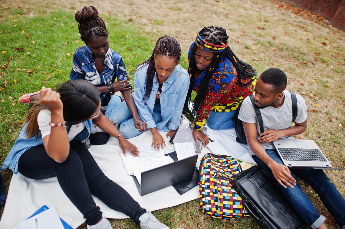 Group of five african college students sit on the ground with their books and laptop