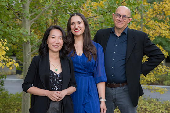 Three people stand together. They are all smiling naturally.