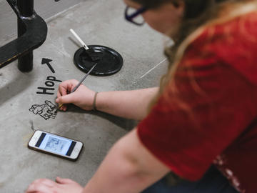A volunteer works from an image on her phone to paint a frog on the landing