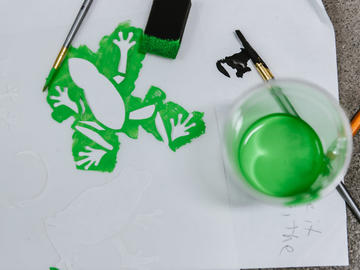 A green frog stencil with a cup of green paint beside it