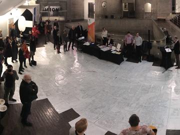 A wide angle photo looking down at the gallery space. People are milled around the edges of the map.