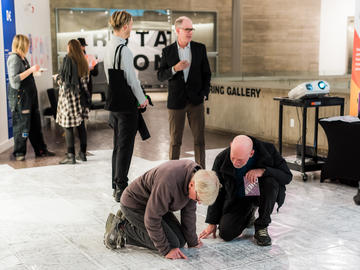 People on their hands and knees study the Queer Map, which is on the floor.