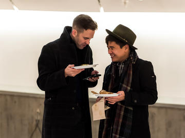 Two peole holding paper plates chat