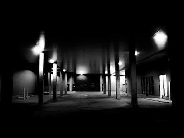 A black and white, slightly blurred image of a building at night showing the entrance to a parking lot or parkade