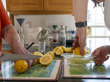 A close up photo of two women's hands as they chop and juice lemons