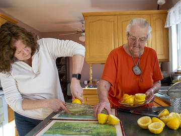 A middle-aged woman juices lemons while an elderly woman gathers up empty rinds of lemons that have already been juiced