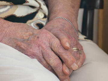 A close-up of an elderly woman's hands, folded in her lap