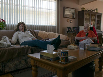 A middle-aged and elderly woman relax together in a living room with a white dog