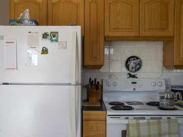 A kitchen with light-coloured wood cabinets. The fridge is sparse with a notepad and several magnets on it.