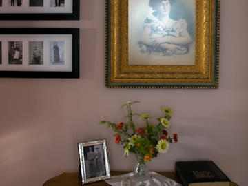 A wall with frames family photos and a side table holding flowers, an old book, and another framed family photo
